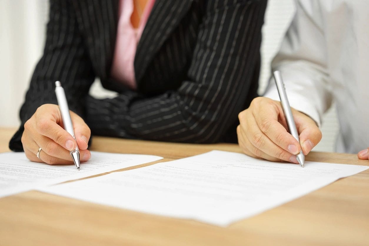 Two people sitting at a table with pens and paper.