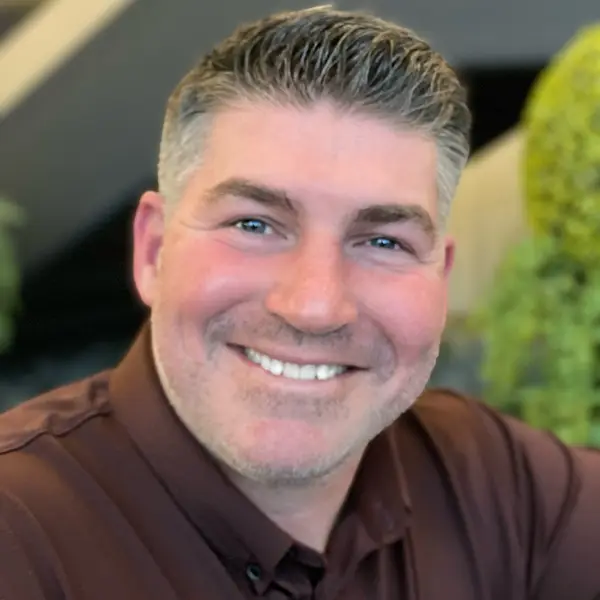 A man with a goatee and brown shirt smiling.