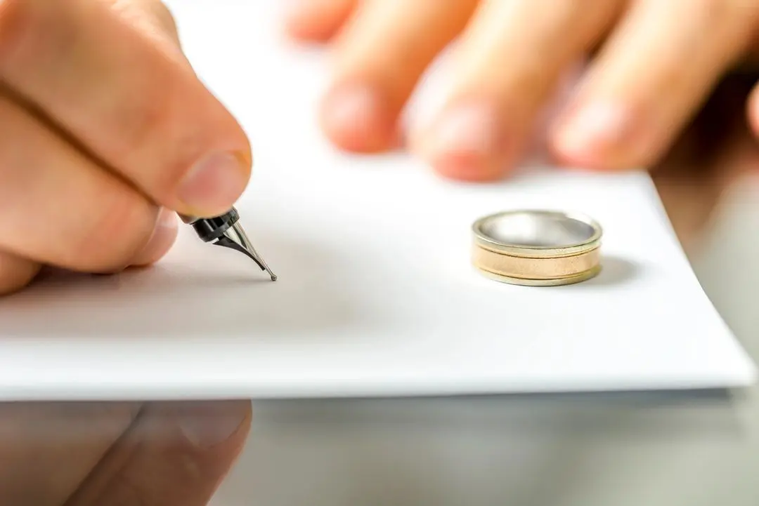 A person writing on paper next to a wedding ring.